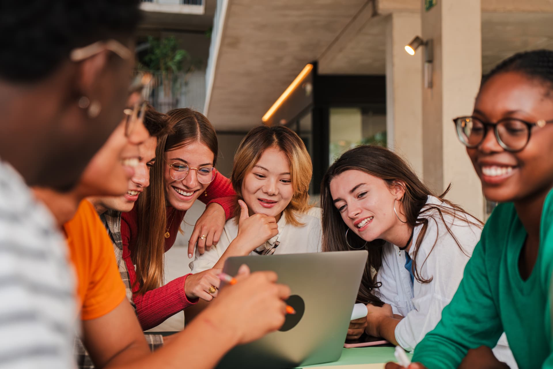 Six young people gathered around a laptop, reacting to what is on screen